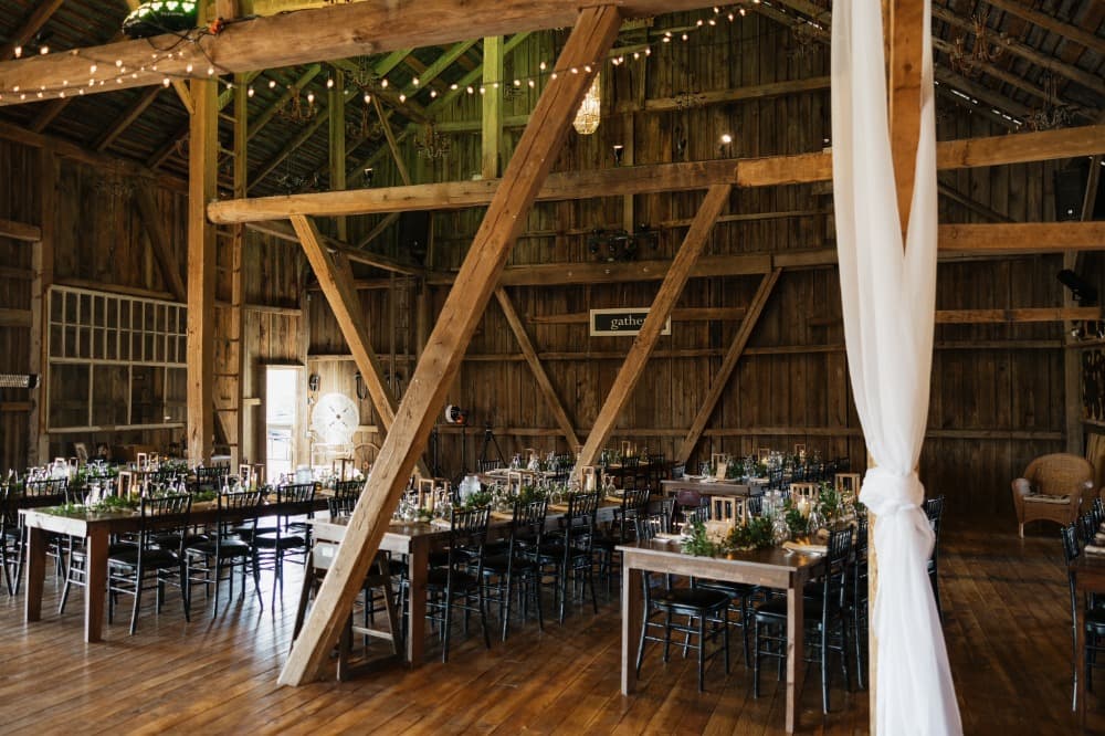 Guest tables arranged across the barn's wide plank floor, with chandeliers and hand-hewn beams overhead.
