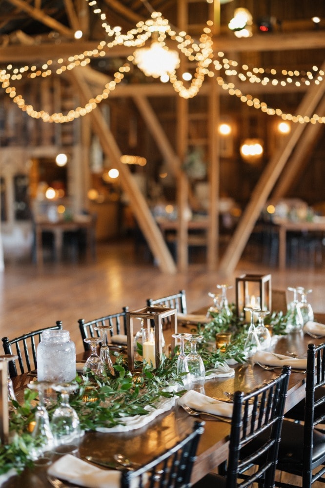 A reception table set with linens, candles and flowers inside the barn.